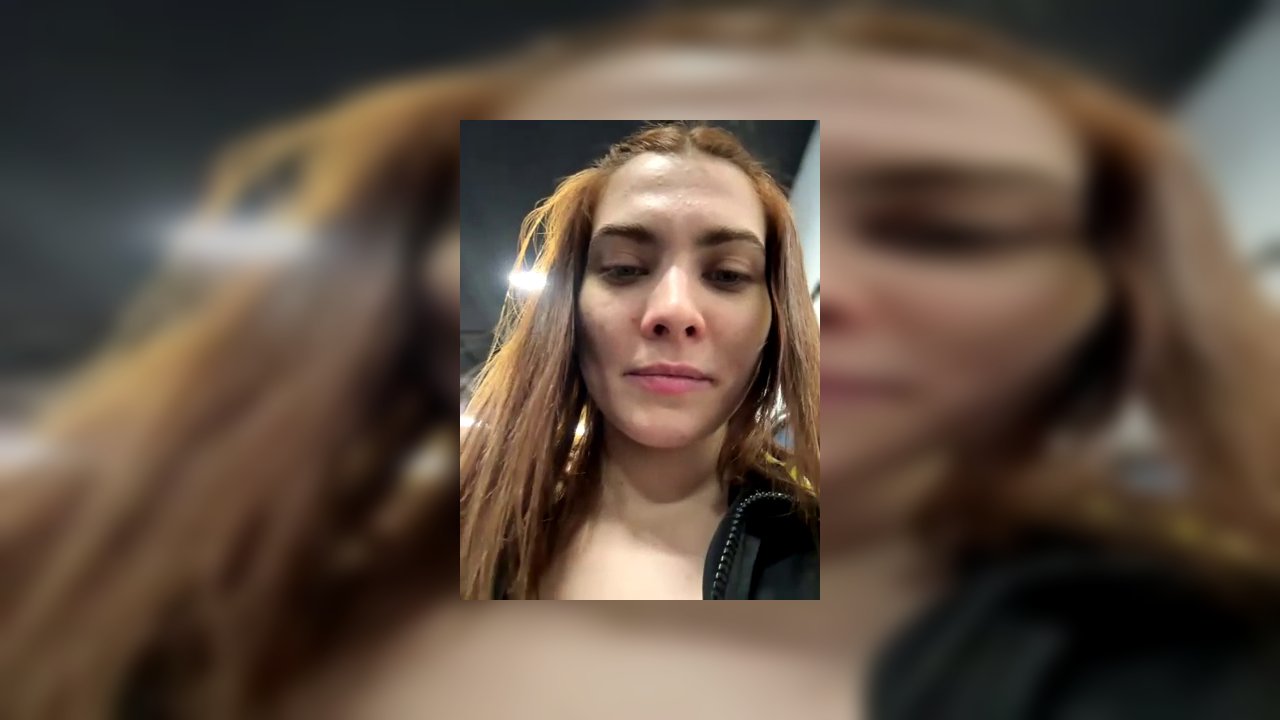 Video of a transgender woman with light skin, red hair, and a tattoo on her thigh. She wears a grey bra and an open black police jacket, exposing her 