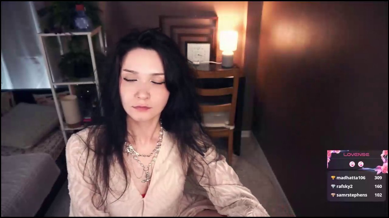 Video of a slender, pale-skinned transgender woman with long black hair in a white lace dress, being kissed passionately by a dark-haired woman in a b