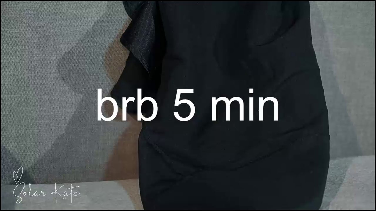 Video of a nude transgender woman with large breasts, light skin, and tattoos, lying on a grey couch, using a dildo.