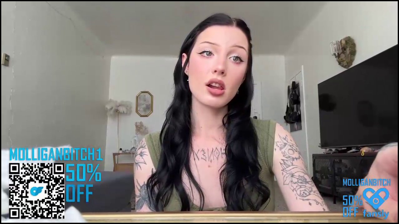 Video of a nude, pale-skinned transgender woman with black hair, lying on a grey couch, with text overlay promoting a MelissaBitch adult video.