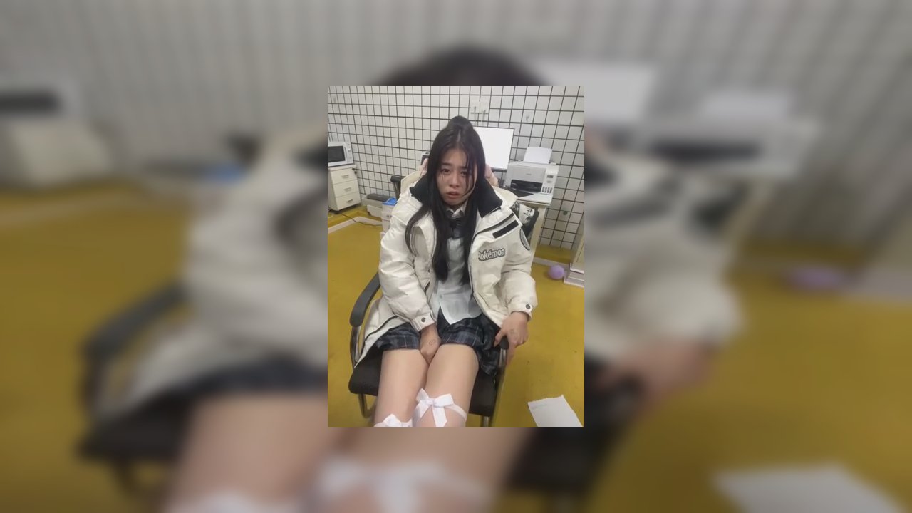 Video of an Asian transgender woman with long black hair, wearing a white jacket, black shorts, and white thigh-high stockings, sitting in a room with